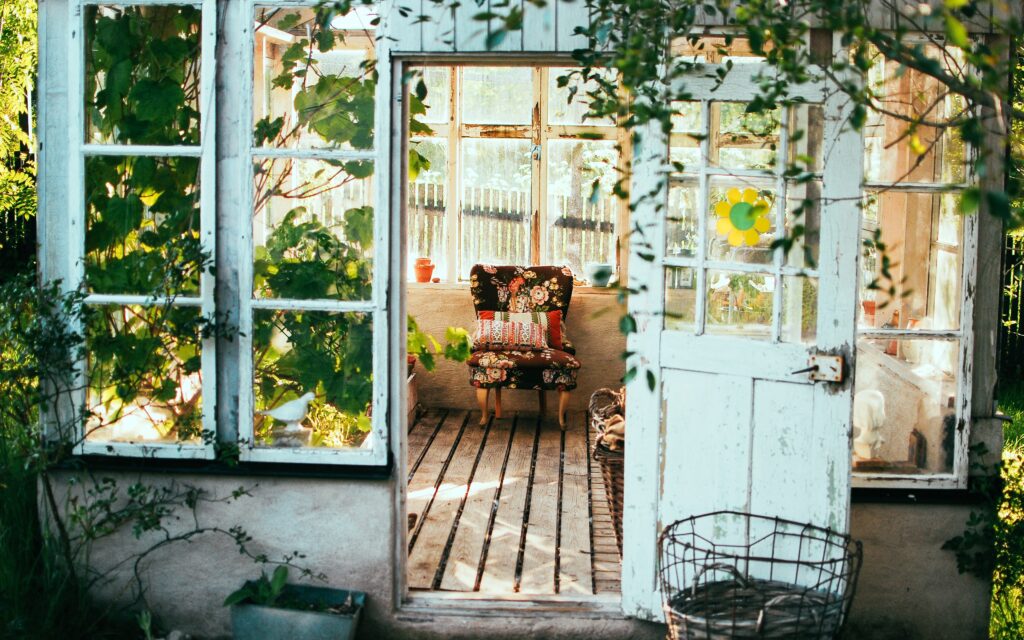 A sunroom greenhouse with plants, light and an empty chair.